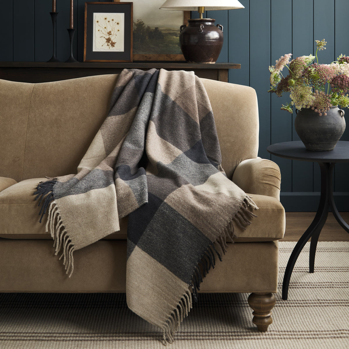Tonic Living Angus Check Mink wool throw blanket draped over a brown velvet sofa in a warm, neutral living room.