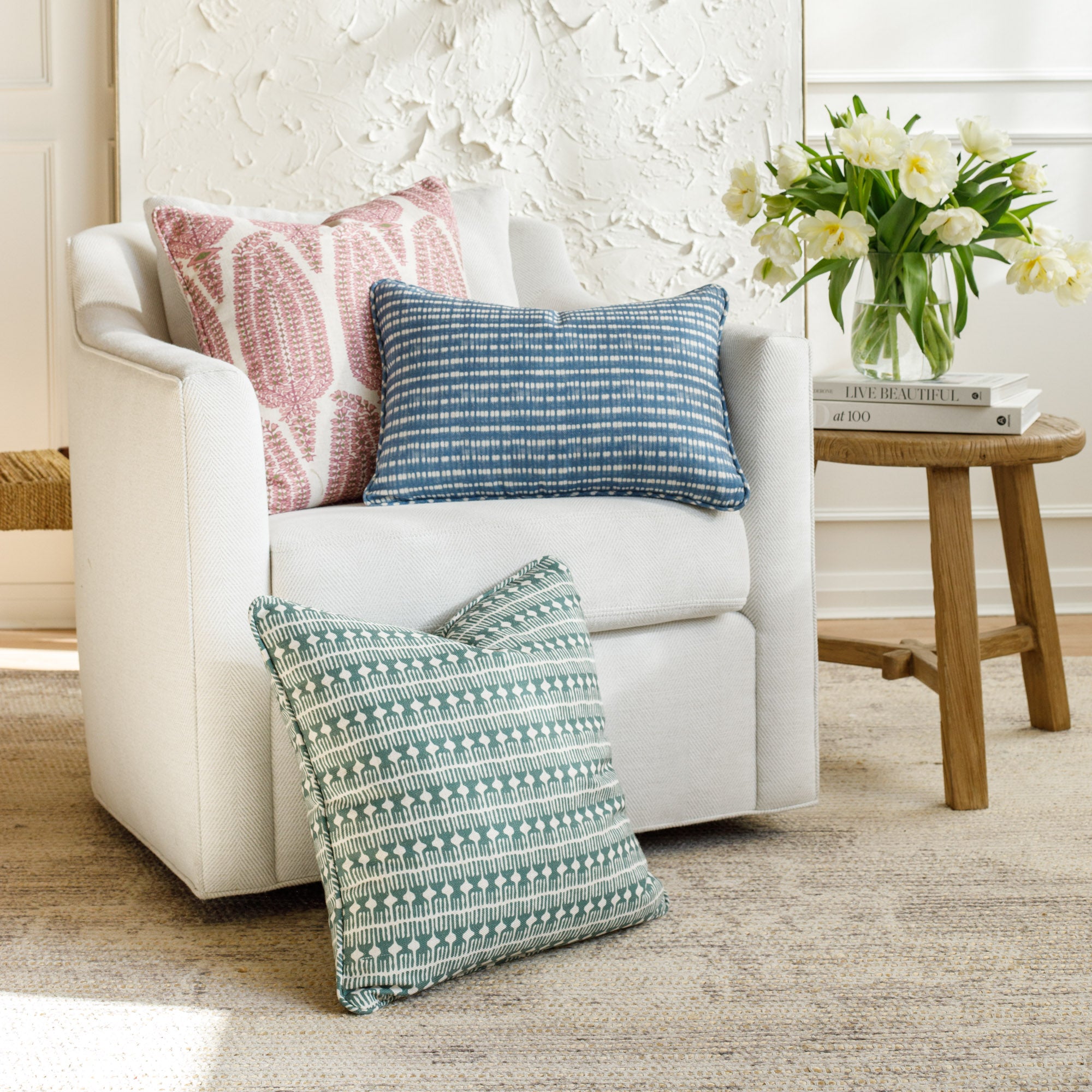 Three throw pillows from the Bombay Collection by Tonic Living—one pink, one blue, and one green—styled on a sofa in a bright, modern living room.