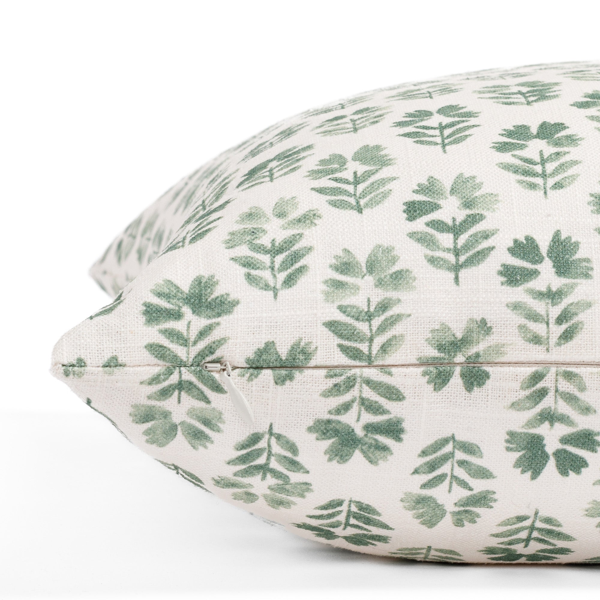 A light green and cream floral block print pillow with a linen texture: close up zipper view.