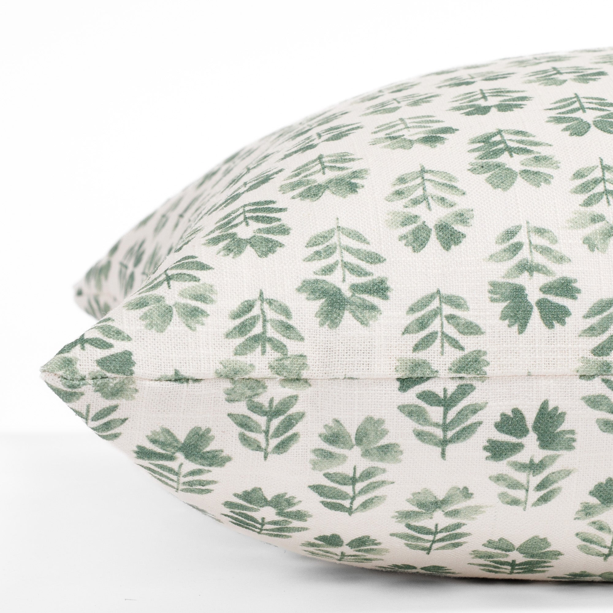A cream designer throw pillow from Tonic Living with light green flowers: a close up side view.
