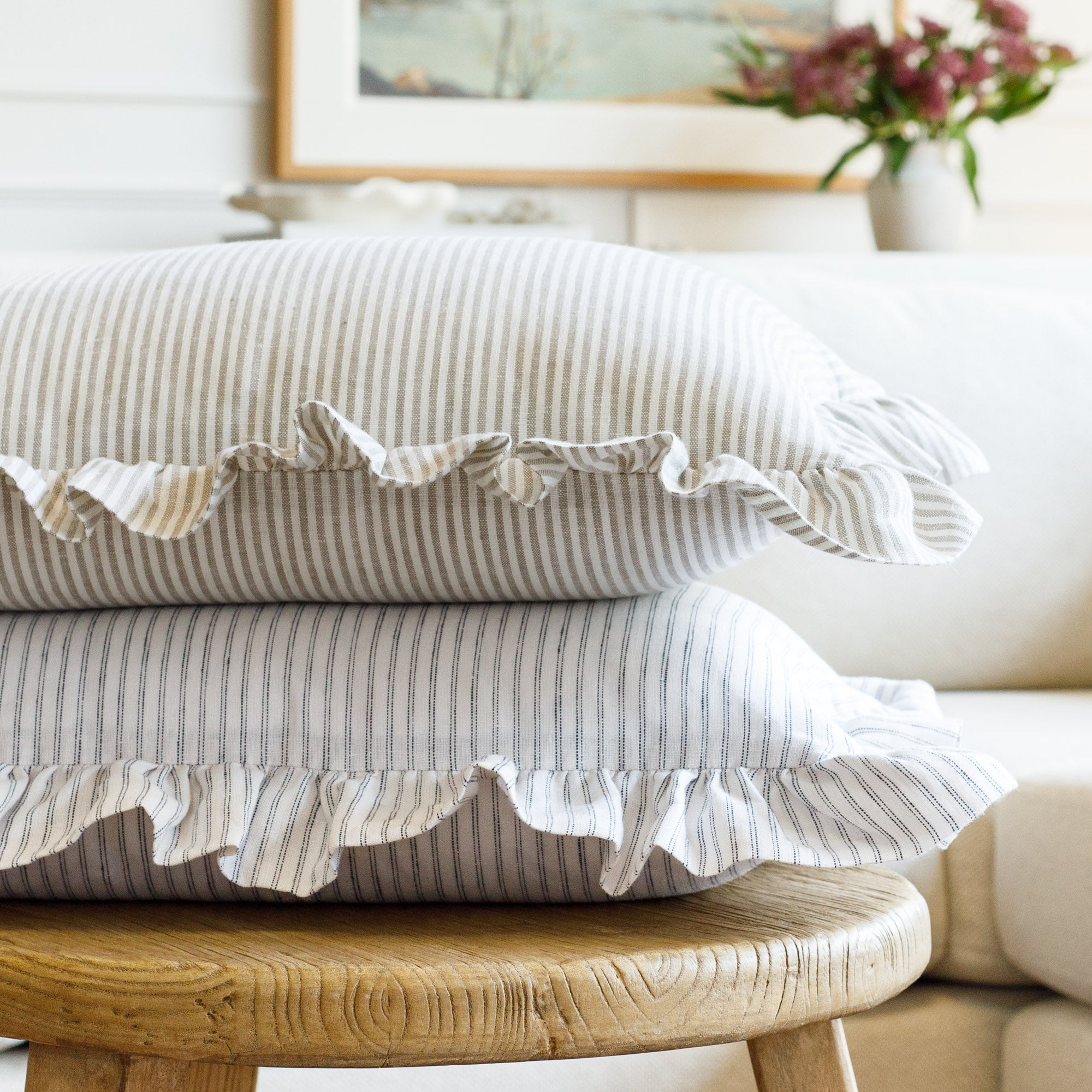 Side view of two ruffle lumbar pillows from Tonic Living stacked, one in warm beige and ivory, the other in creamy white and black—highlighting their soft linen textures and timeless appeal.