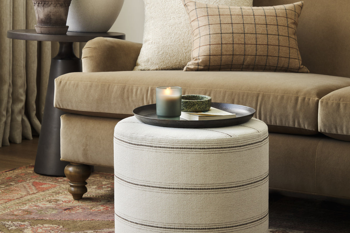 Tonic Living Gibson Stripe Birch round ottoman styled as an accent table in a warm neutral living room with coordinating throw pillows.
