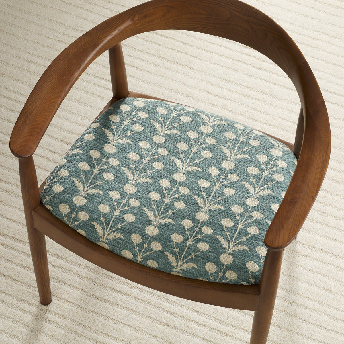 Tonic Living Hazel Pool botanical upholstery fabric shown on a dining chair seat in muted blue-green and beige.
