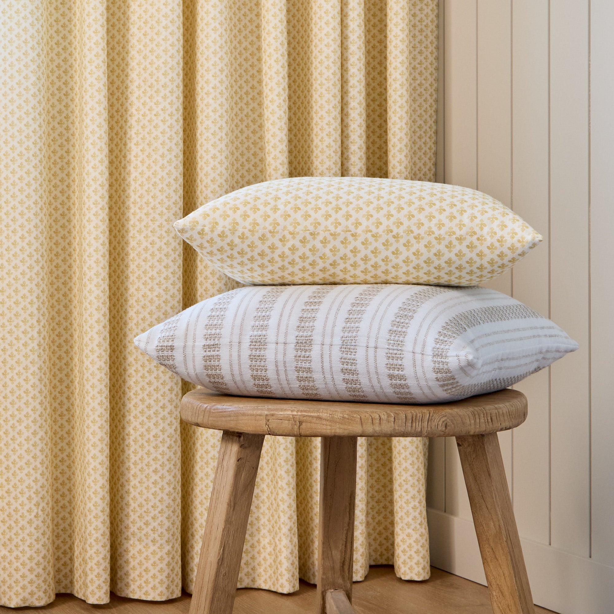 Lyra Butter Yellow lumbar pillow stacked with Briar Stripe 20x20 Pillow, Wheat by Tonic Living in front of coordinating Lyra curtain fabric.