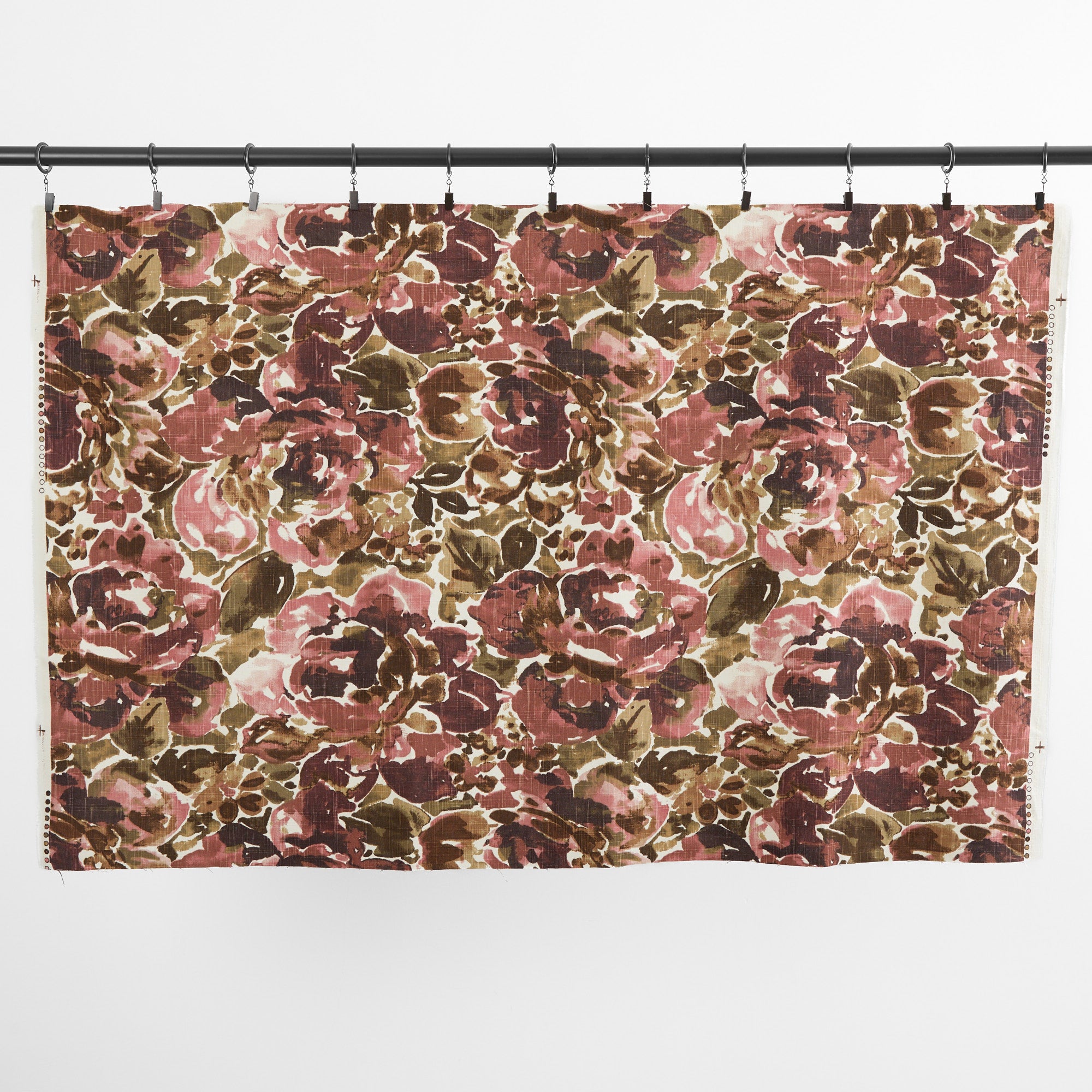 One yard of Tonic Living Marbella Rose floral fabric hanging from clips, showing the full-scale burgundy and pink abstract pattern.