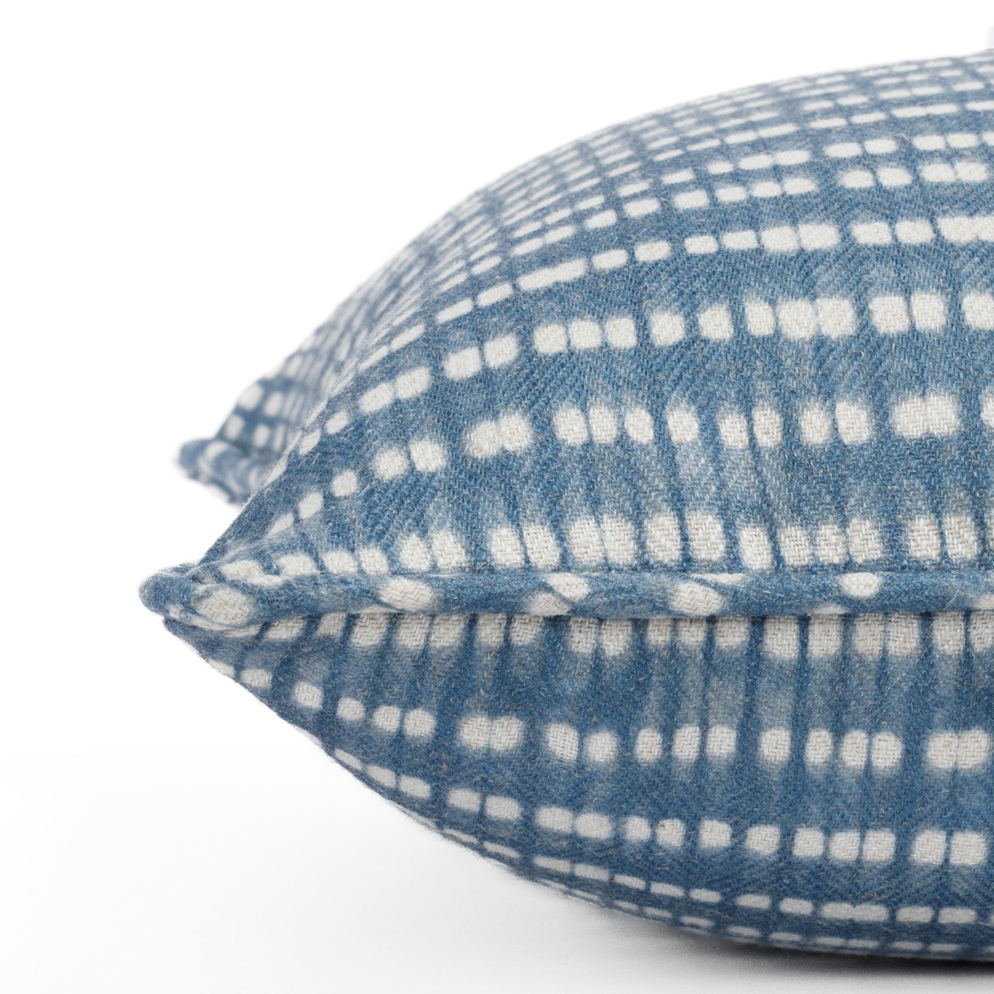 Close-up side view of a chambray blue and white pillow with piped detail and dotted stripe pattern (Nile Indigo from Tonic Living).