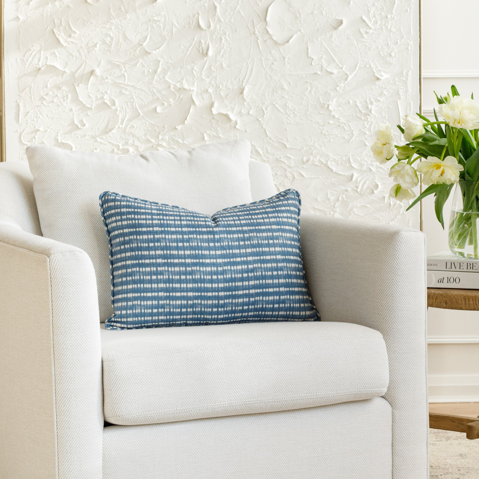 14x20 blue and white lumbar pillow with a dotted stripe pattern and piping detail, styled on a white chair (Nile Indigo by Tonic Living).