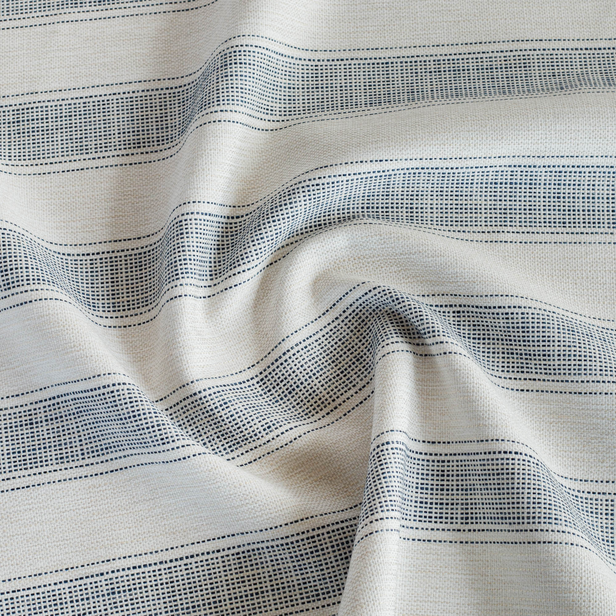Revitalize Denim, an indoor/outdoor upholstery fabric from Tonic Living, featuring wide-set vertical navy blue stripes with woven running stitches.