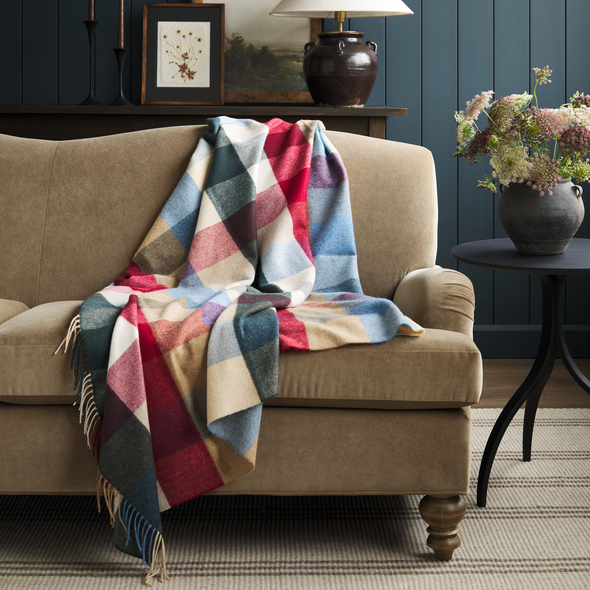 Tonic Living Rowan Check Orchard wool throw blanket styled over a warm brown velvet sofa, featuring a colourful oversized check pattern.
