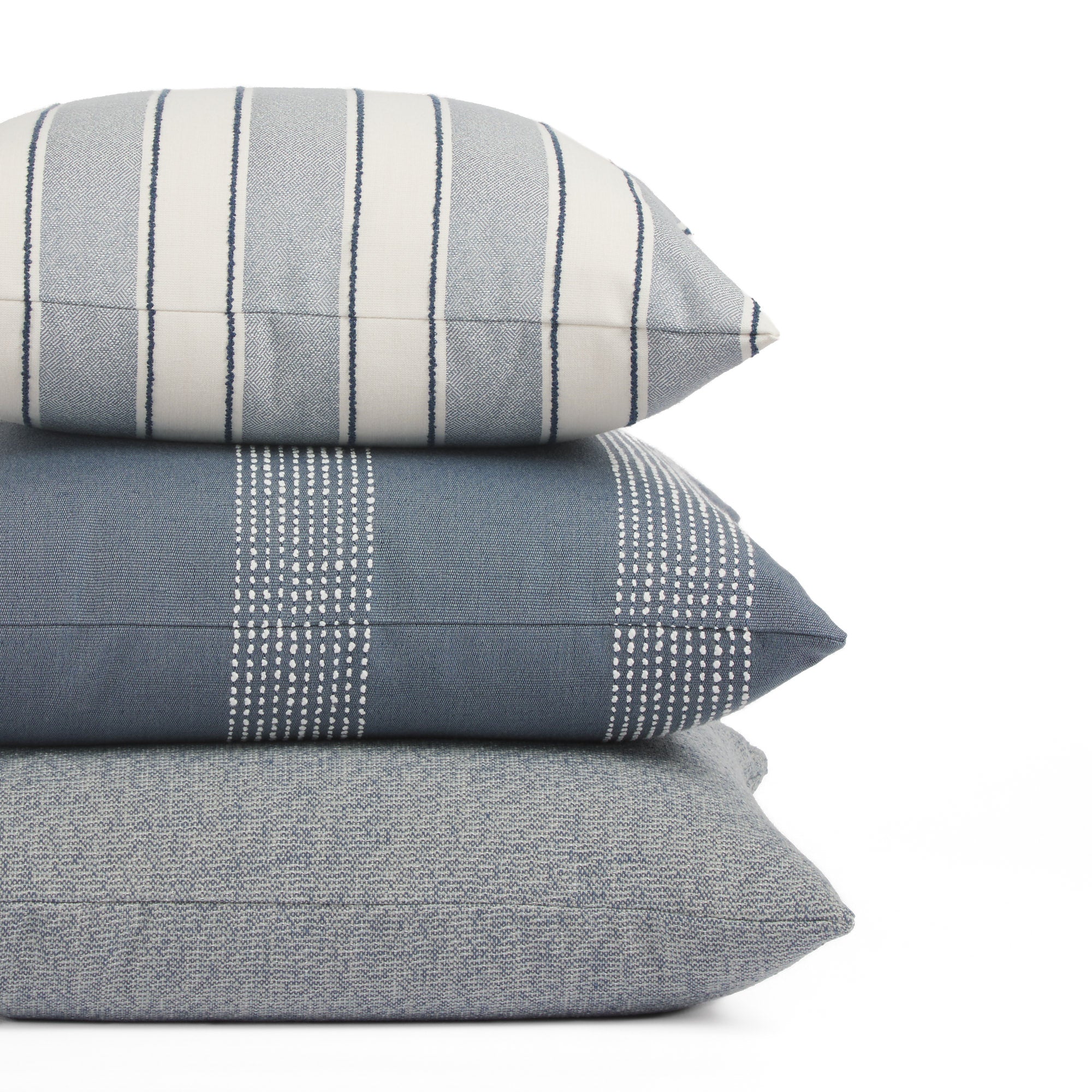 Stack of Tonic Living outdoor pillows including Sentiment Denim, Caper Slate, and Troy Denim in blue striped designs.