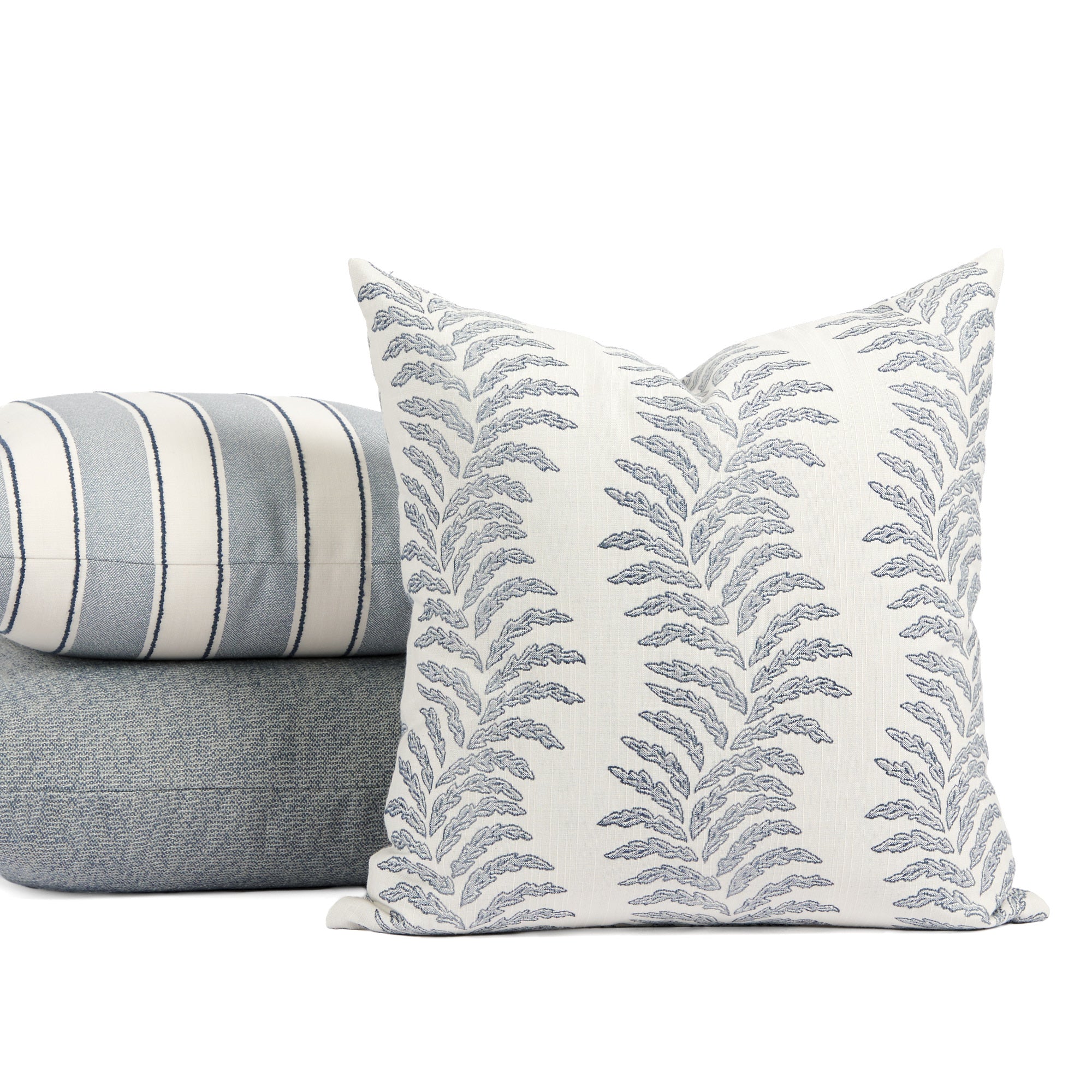 Tonic Living Swoon Denim throw pillow styled in front of a stack of blue toned outdoor pillows.
