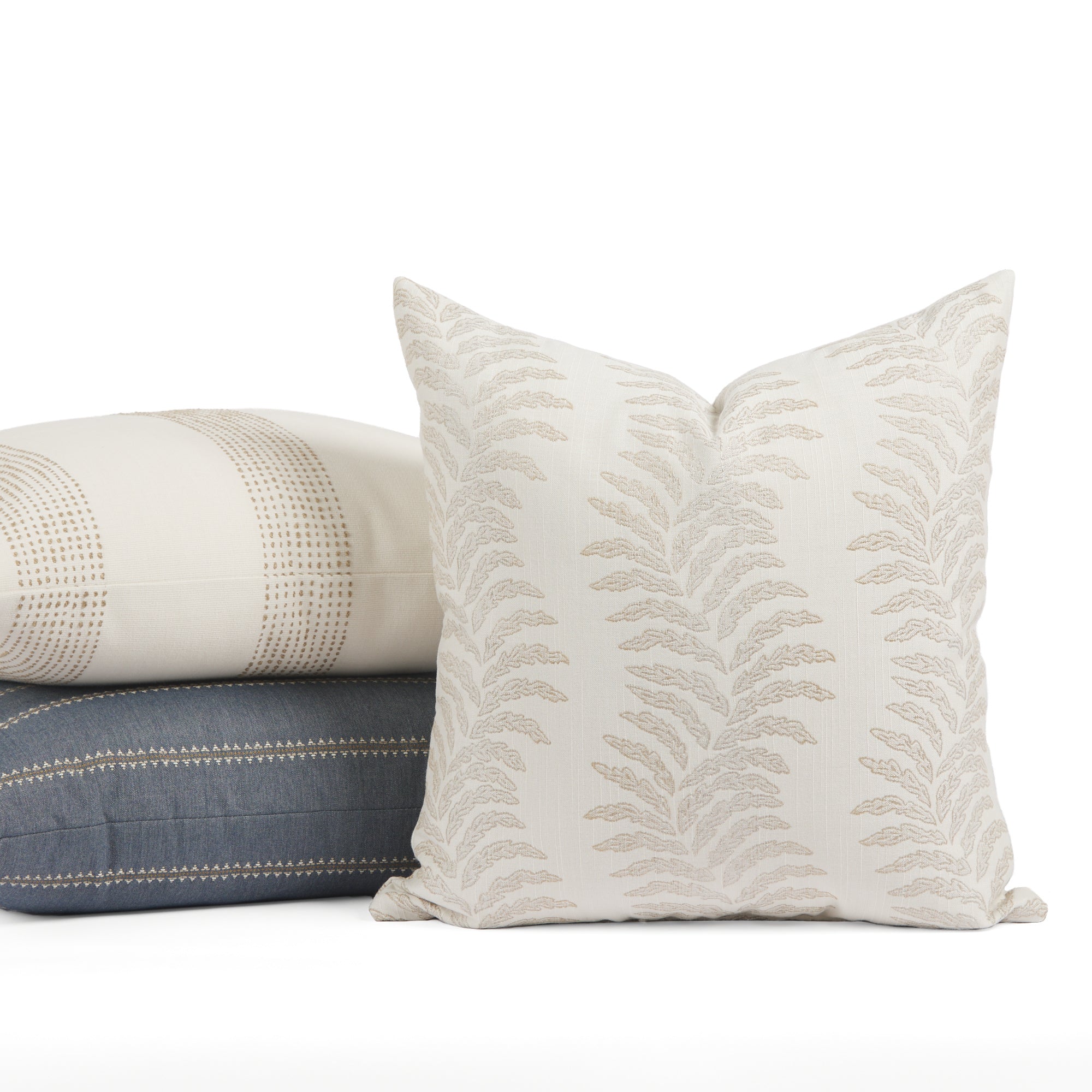 Tonic Living Swoon Sand outdoor cushion styled in front of cream and blue throw pillows.