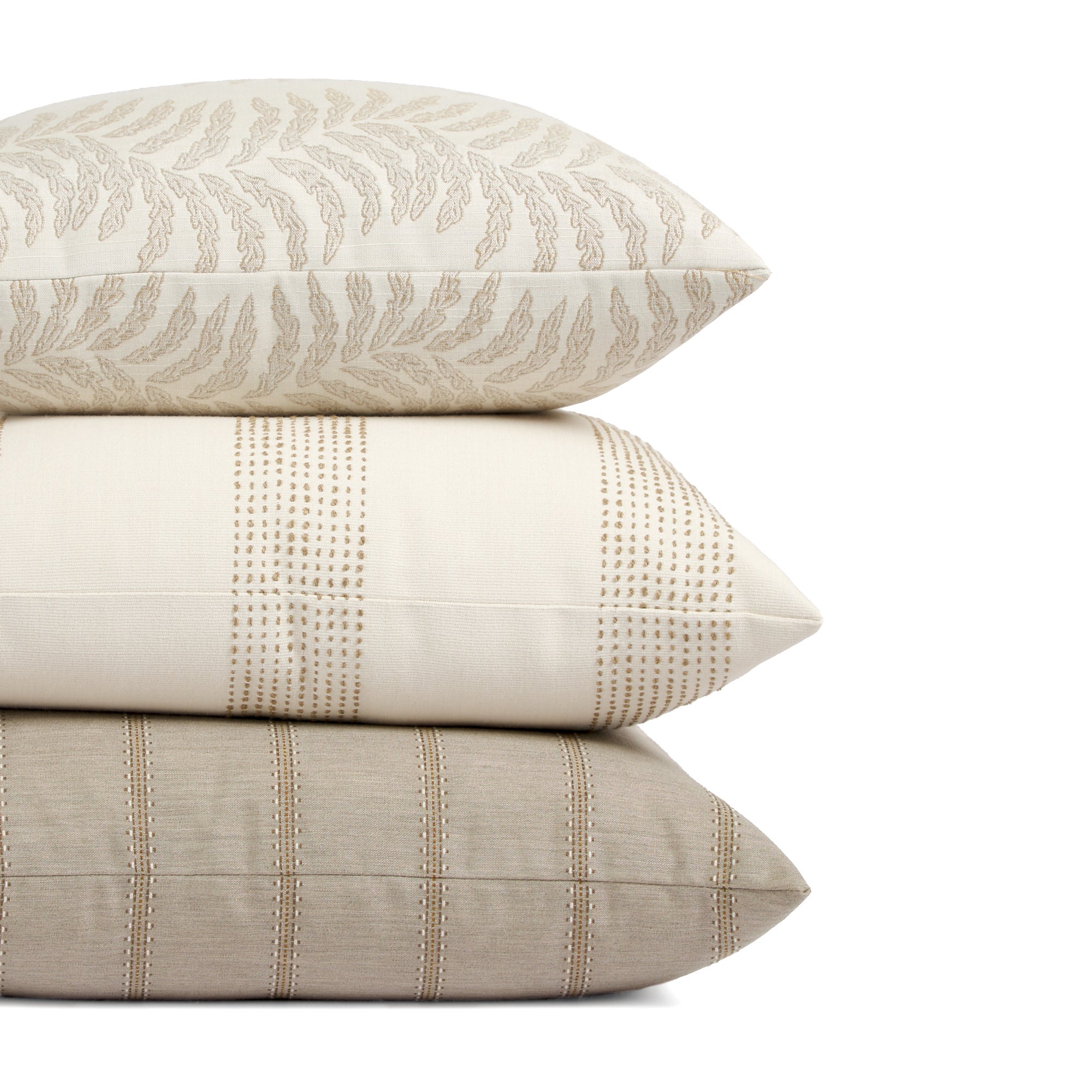Stack of Tonic Living outdoor pillows including Swoon Sand, Caper Linen, and Talisman Sand in neutral tones.