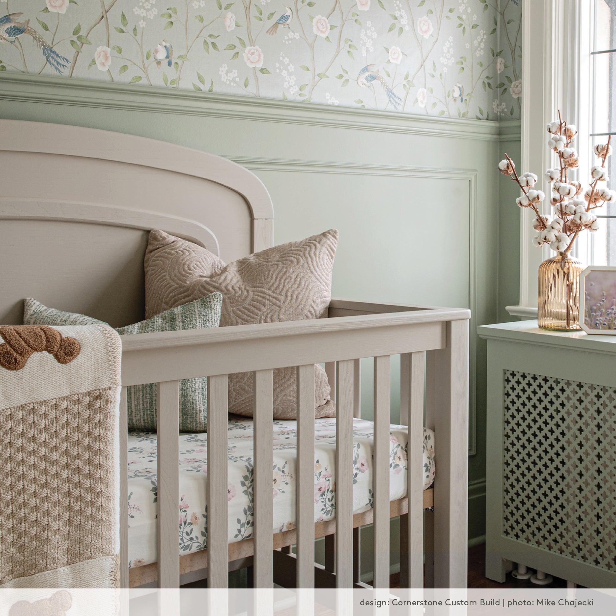Pastel green nursery with floral wallpaper and an earthy pink pillow.