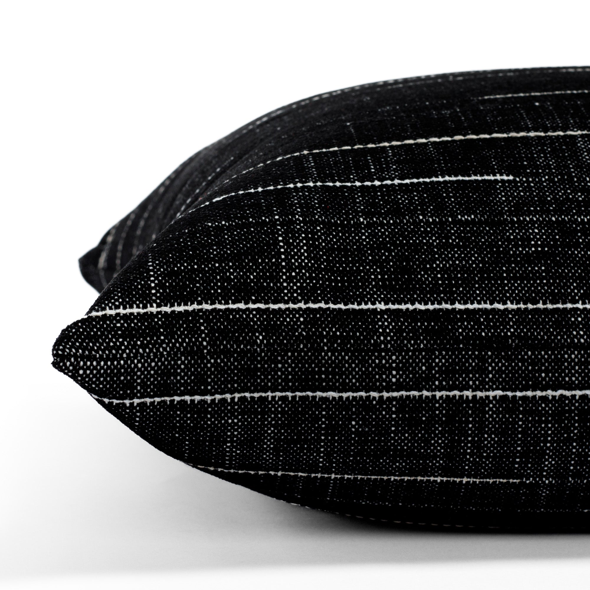 Yuzu Onyx, a black and white indoor/outdoor pillow from Tonic Living, showcasing a dappled texture accented with organic white stripes: close-up side view.