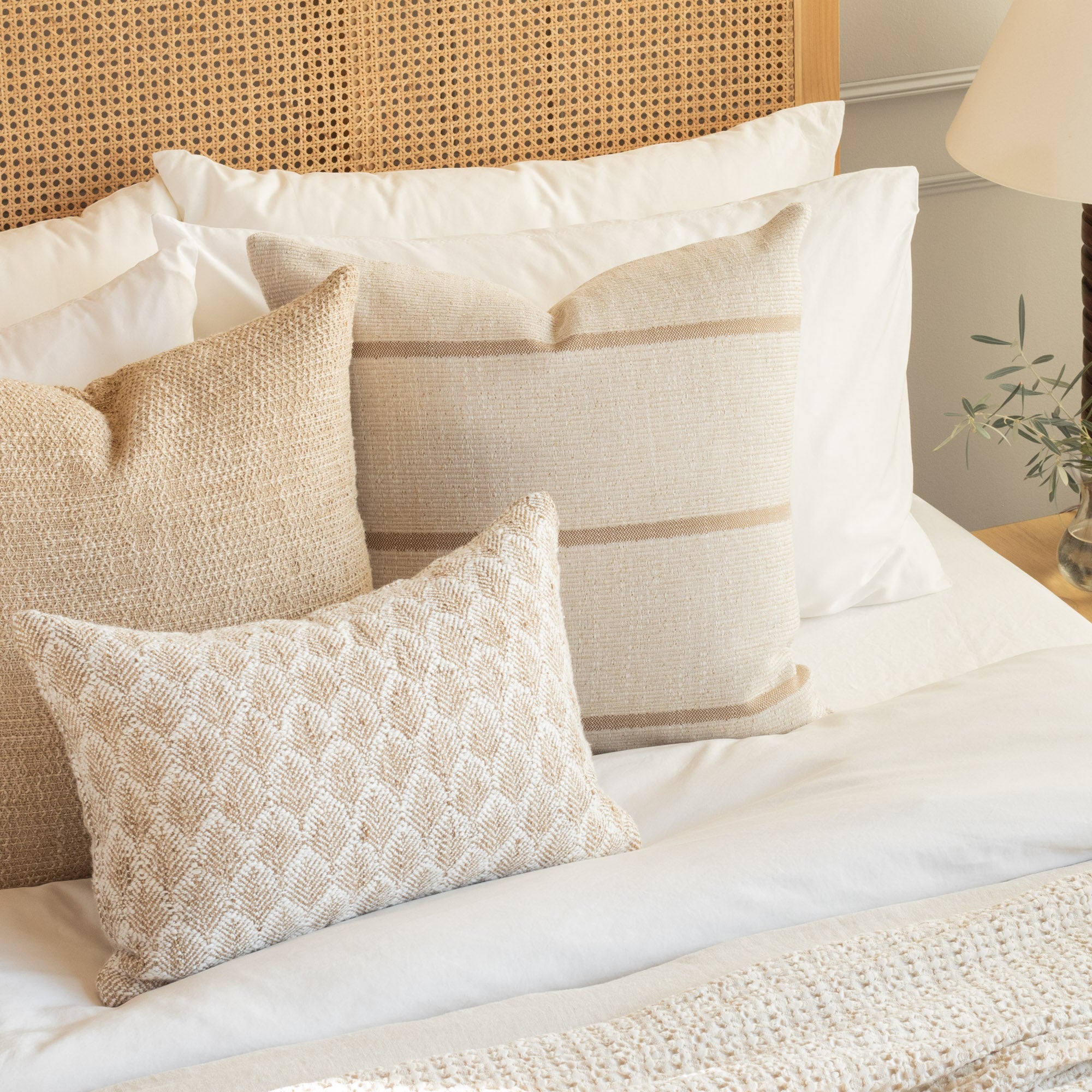 A selection of neutral, textured Tonic Living cushions styled on a bed.