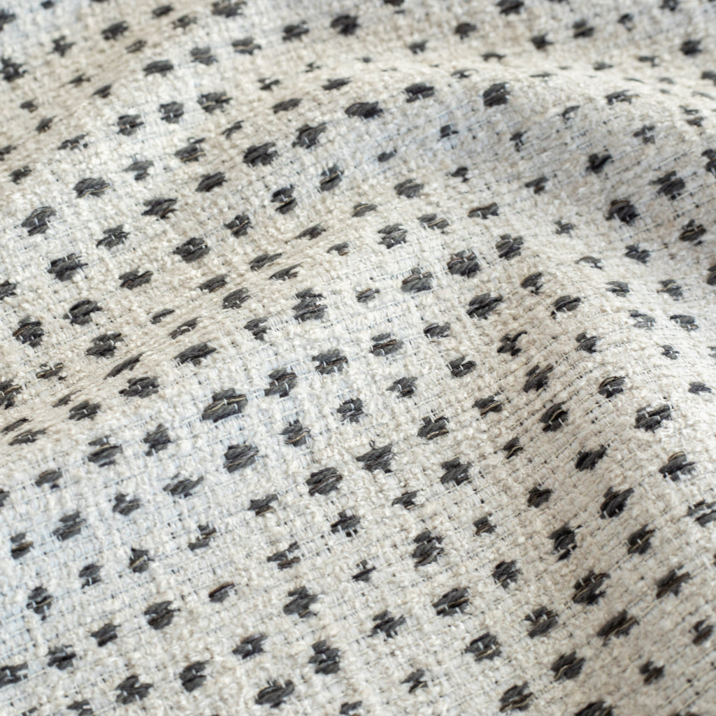 an off-whitee and black variegated polka-dot patterned textured home decor fabric : close up view