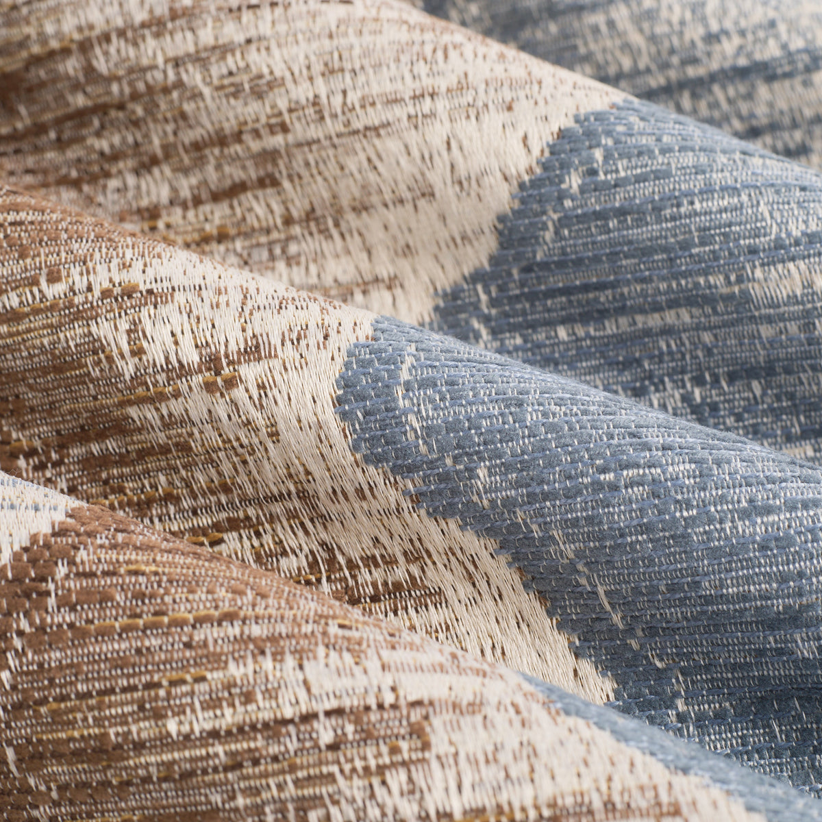 Close up of Tonic Living Cortina Storm fabric showing its textured jacquard weave in chambray blue, coffee brown, golden brown, and parchment.