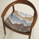 Tonic Living Cortina Storm abstract upholstery fabric shown on a dining chair seat in layered blue and brown tones.