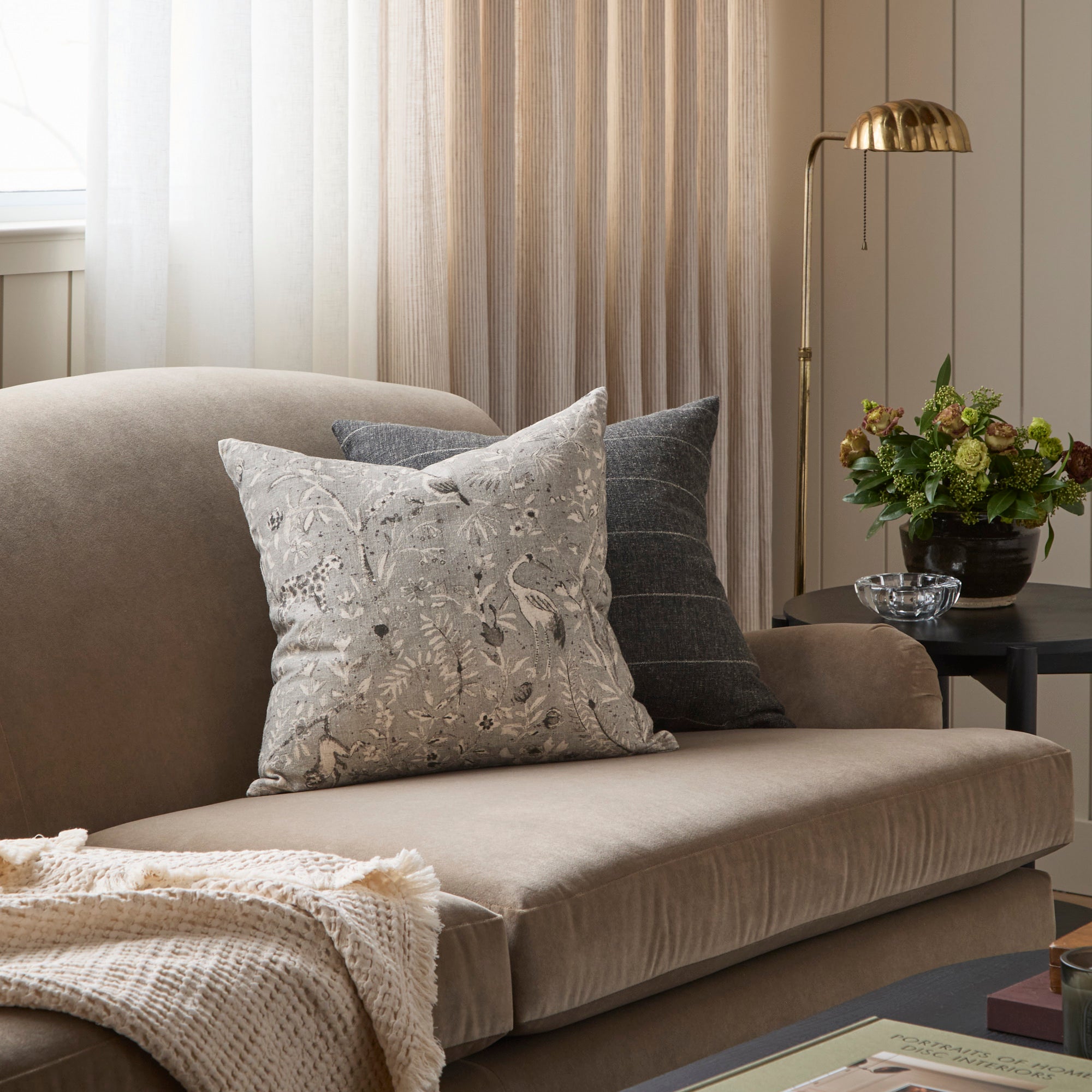 A pair of vintage style throw pillows from Tonic Living, styled on a brown velvet sofa.