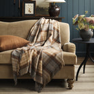 Tonic Living Duncan Plaid Tweed wool throw blanket styled over a warm brown velvet sofa, featuring a classic brown, camel, and grey plaid.