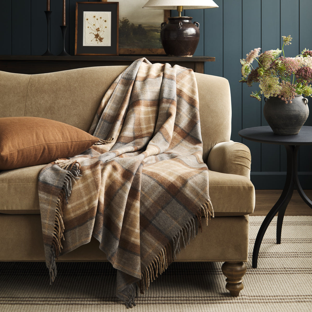 Tonic Living Duncan Plaid Tweed wool throw blanket styled over a warm brown velvet sofa, featuring a classic brown, camel, and grey plaid.
