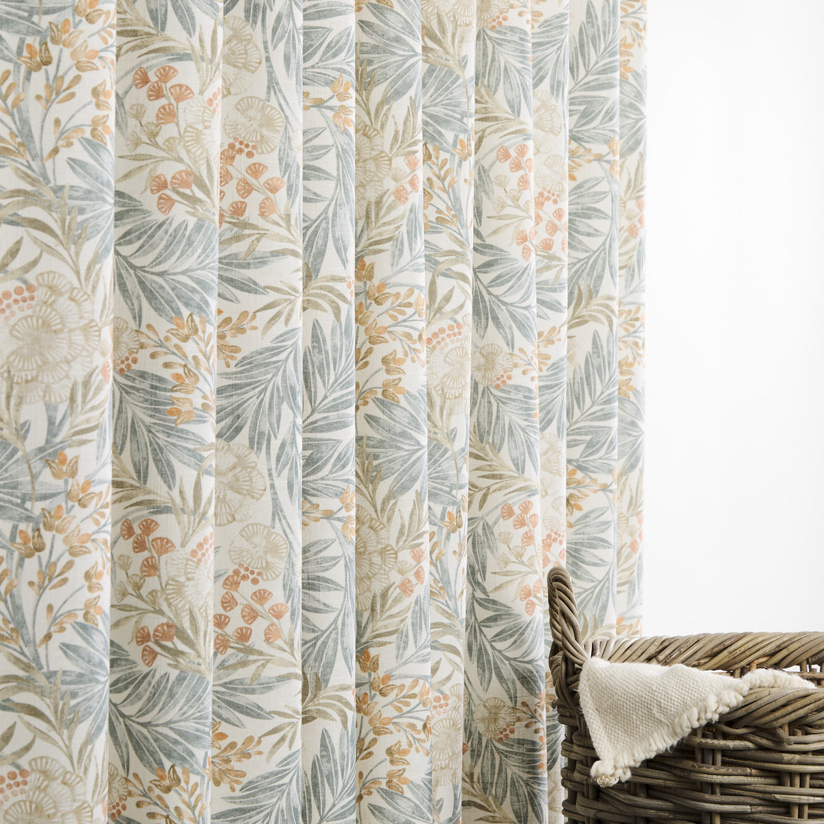 Tonic Living Fable Meadow botanical drapery fabric shown as curtains featuring leafy blue, terracotta, and brown motifs on a soft white ground.