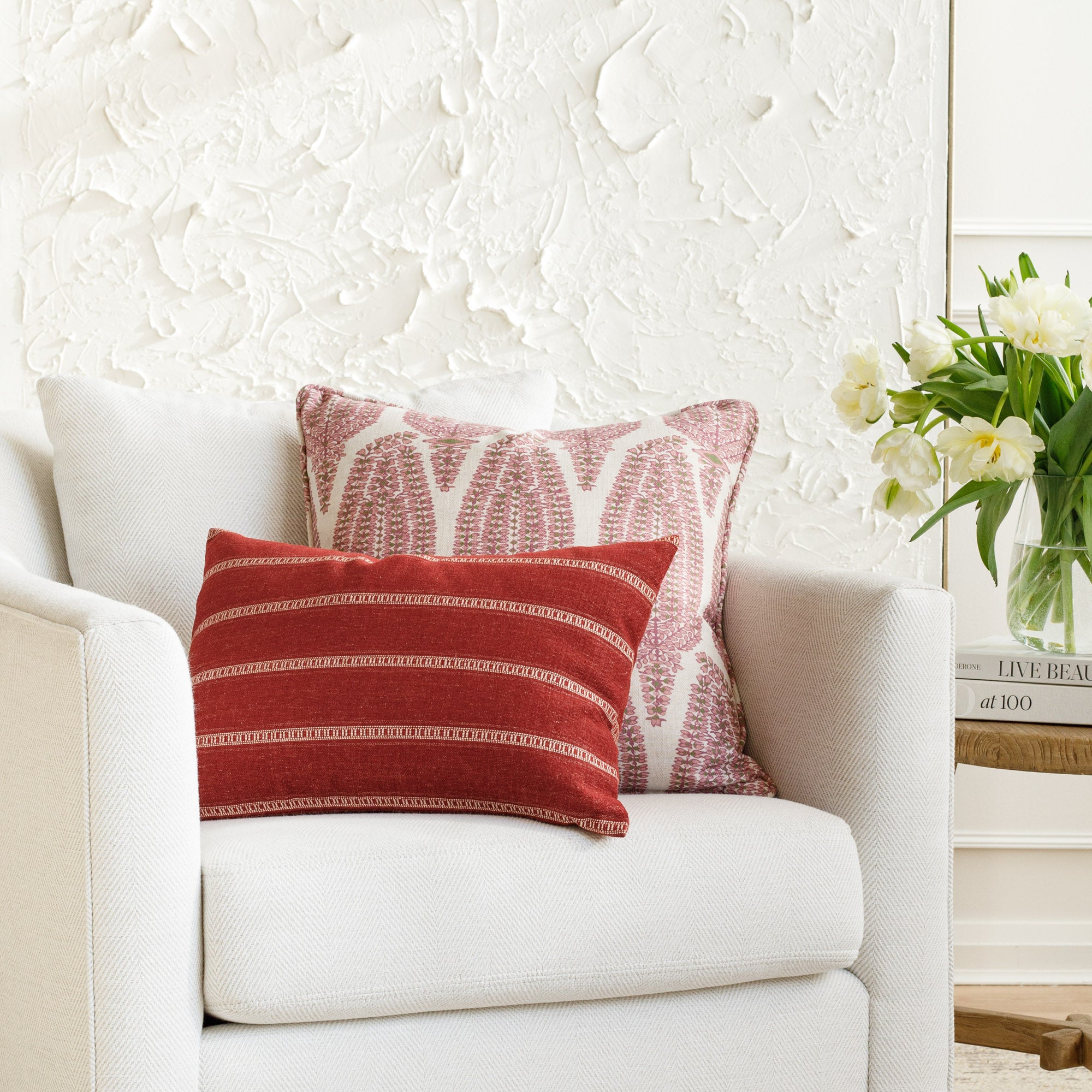 Two designer throw pillows styled on a white chair: Georgia Orchid Pink in a soft blush, paired with the vivid red and white Brunswick Stripe Pomegranate pillow from Tonic Living, creating a vibrant and colorful look.