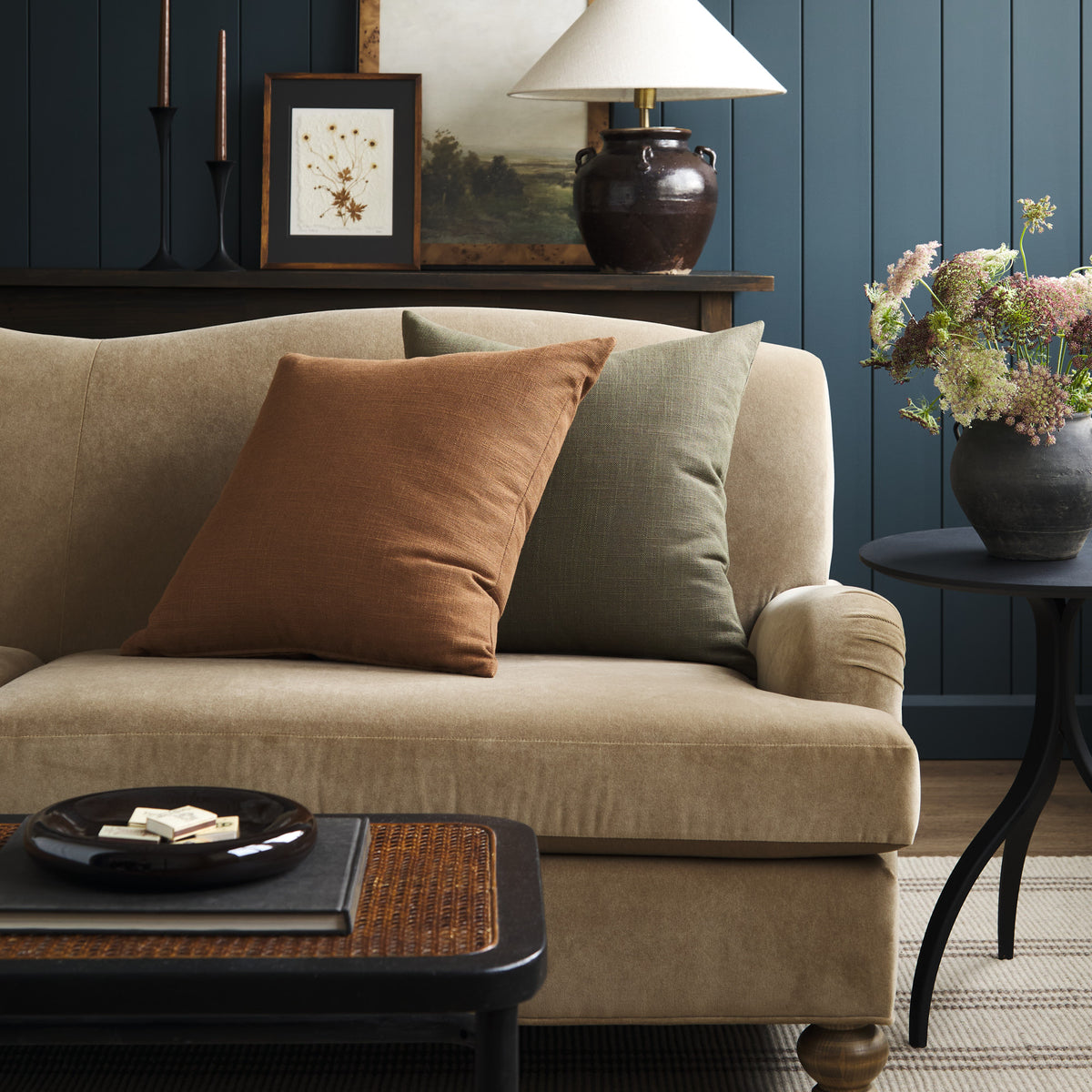 Tonic Living Hampton pillows in Moss earthy green and Cinnamon russet brown styled on a sofa in a moody living room.
