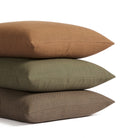 Stack of Tonic Living Hampton pillows in Cinnamon russet brown, Moss earthy green, and Walnut dark brown with linen-inspired texture.