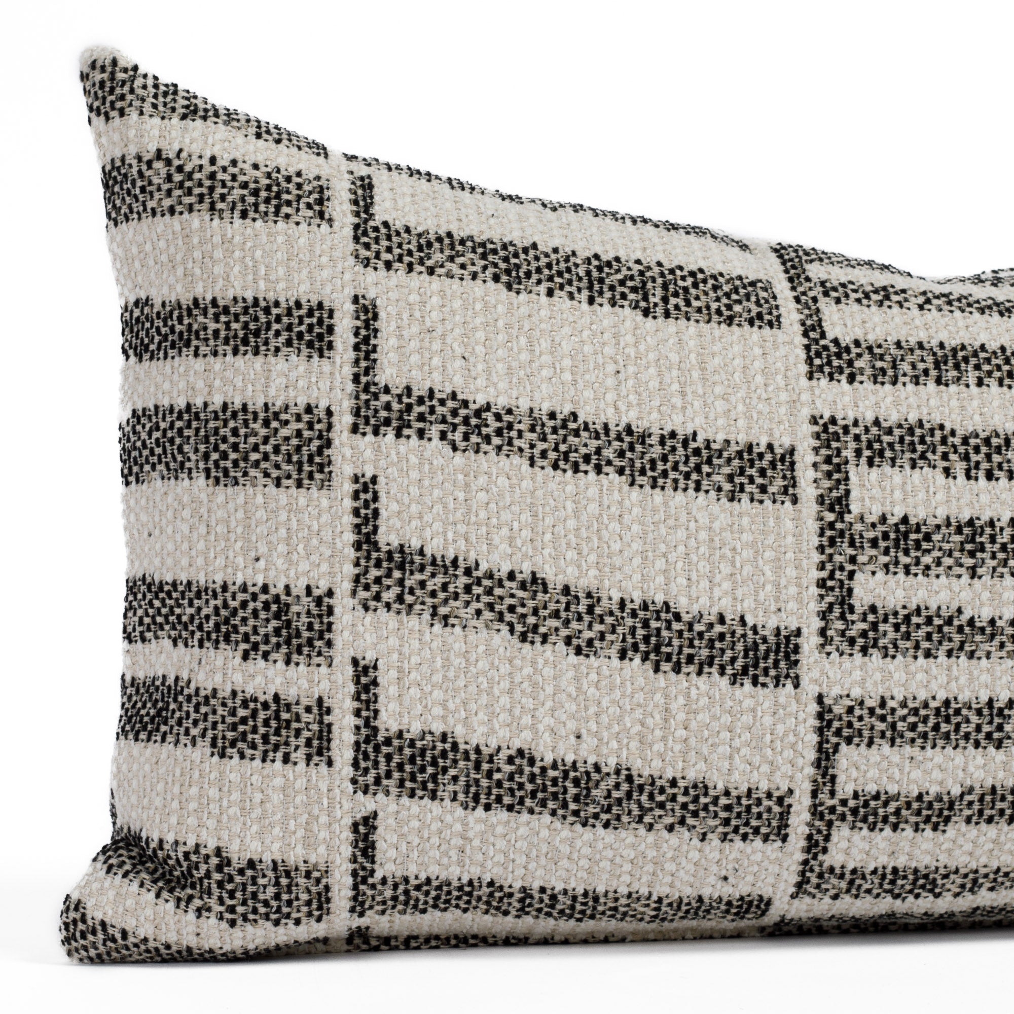 Close-up of the Mallia Carbon 12x24 decorative outdoor lumbar cushion by Tonic Living, showcasing the organic black pattern and luxurious woven texture in off-white and beige tones.
