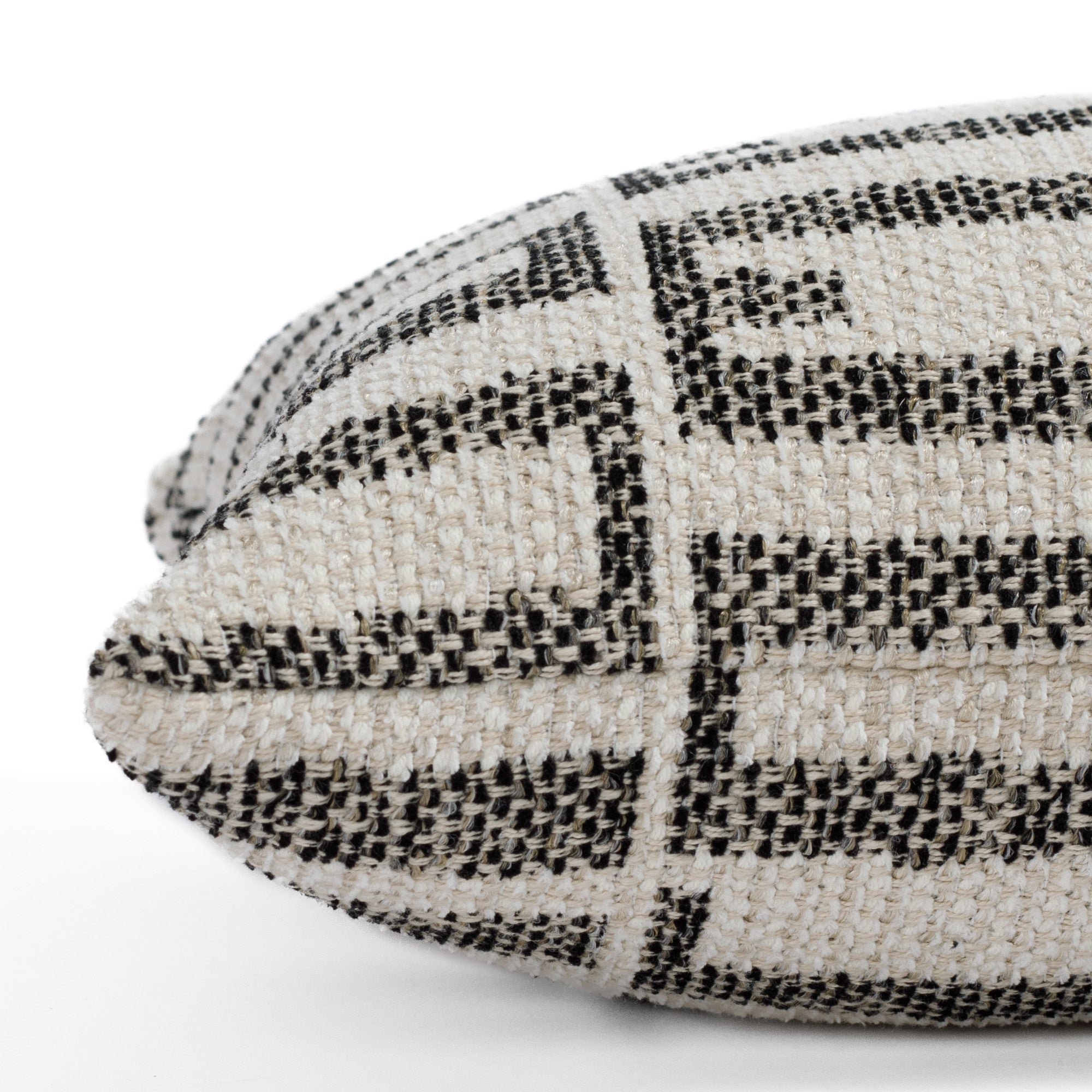 Close up side view of the Mallia Carbon 12x24 lumbar (small bolster pillow) from Tonic Living, emphasizing the soft woven texture and stain-resistant black and sand-toned geometric design.