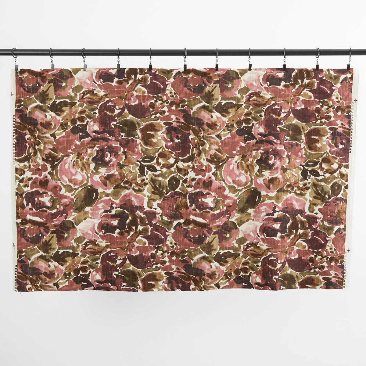 One yard of Tonic Living Marbella Rose floral fabric hanging from clips, showing the full-scale burgundy and pink abstract pattern.