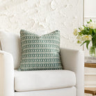Spruce green and white pillow with a modern global pattern and piping detail, styled on a white chair (Meadow Emerald by Tonic Living).
