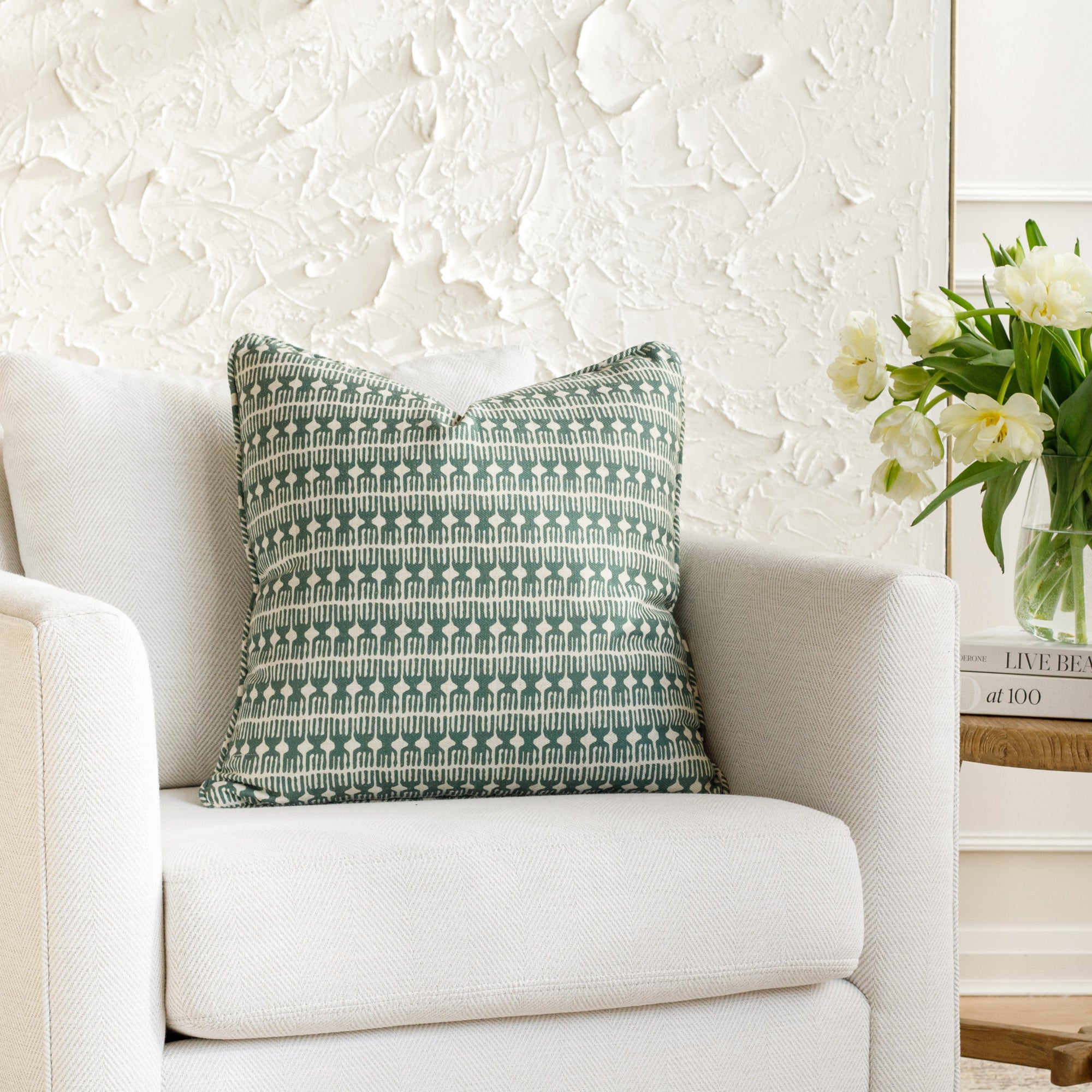 Spruce green and white pillow with a modern global pattern and piping detail, styled on a white chair (Meadow Emerald by Tonic Living).