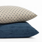A beige and navy patterned pillow resting on a navy textured stripe pillow.