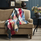 Tonic Living Rowan Check Orchard wool throw blanket styled over a warm brown velvet sofa, featuring a colourful oversized check pattern.