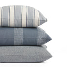 Stack of Tonic Living outdoor pillows including Sentiment Denim, Caper Slate, and Troy Denim in blue striped designs.