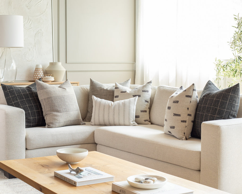 Earthy warm charcoal and cream sectional pillow pairing: a collection of charcoal and cream pillows in an array of textured patterns including stripes, an abstract brushstroke and windowpane check.