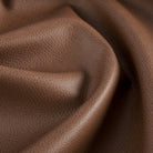Close up of Tonic Living Smythe Cognac faux leather upholstery fabric showing its deep cognac brown colour and realistic leather grain.