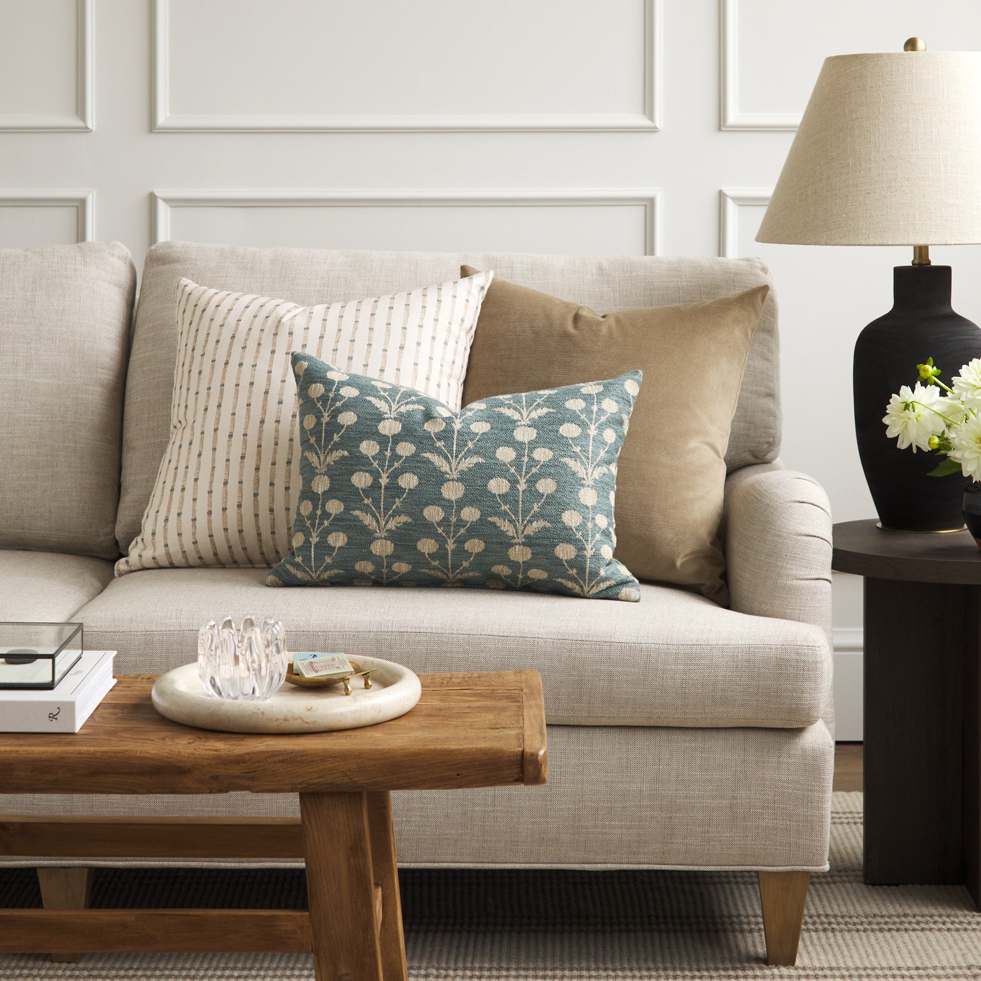 Tonic Living Hazel Pool botanical lumbar cushion styled on a sofa with a neutral striped pillow and warm brown velvet pillow.
