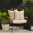 Tonic Living Swoon Terracotta throw pillow styled on a chair with the Talisman Sand 22x22 cushion outdoors.