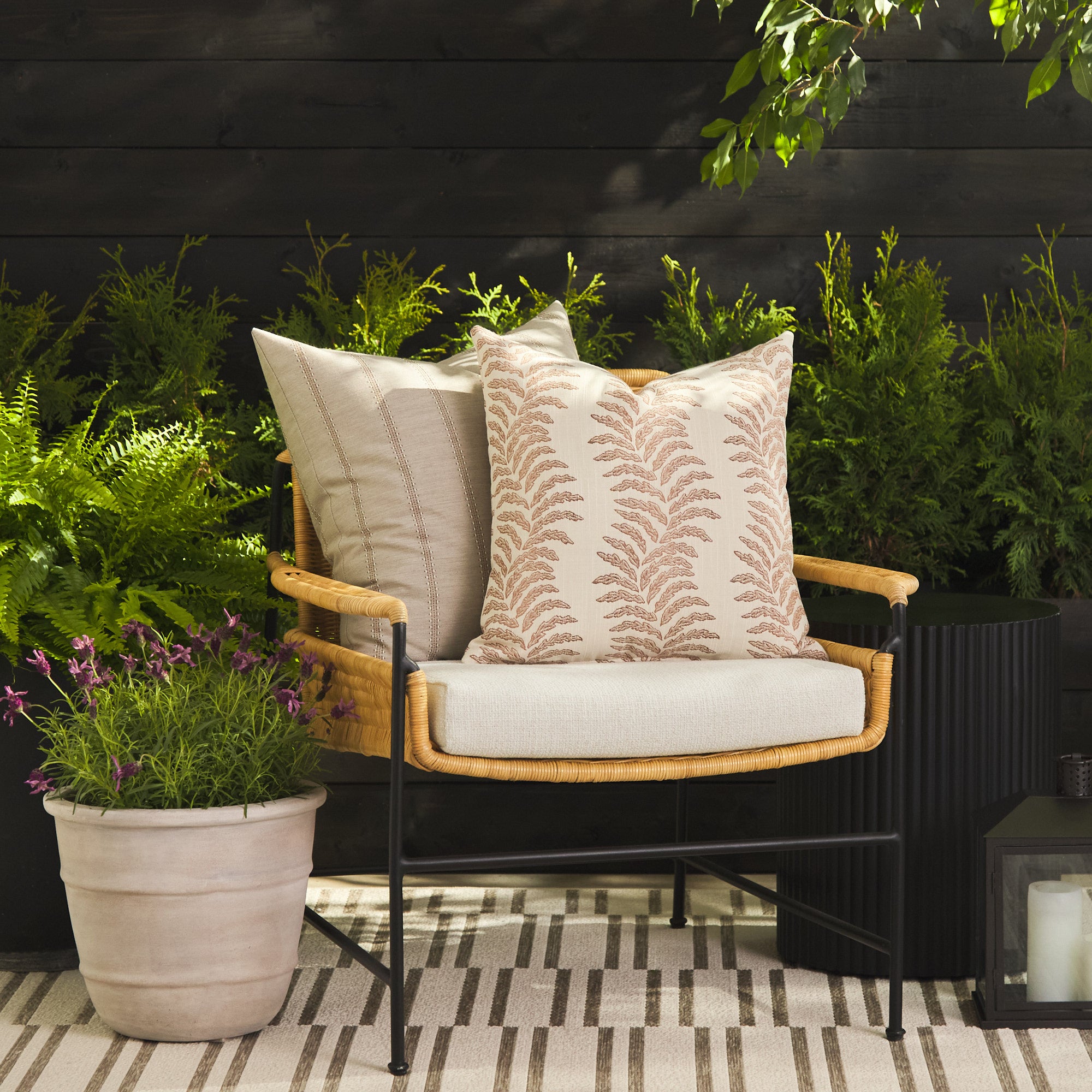 Tonic Living Swoon Terracotta throw pillow styled on a chair with the Talisman Sand 22x22 cushion outdoors.