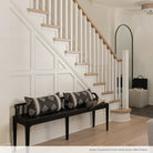 A contemporary black wood bench in a front hall with a white oak staircase and wall moulding. 