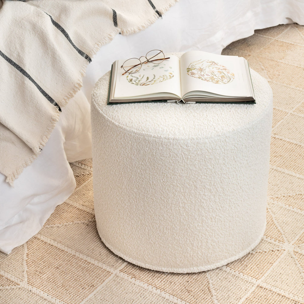 Cambie Boucle Round Ottoman Chalk with a book, used as a bed side table