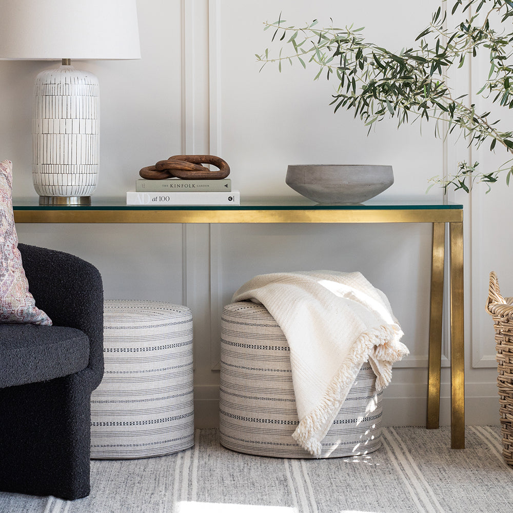 modern farmhouse style: ottomans under a brass console with a cream throw and olive tree.