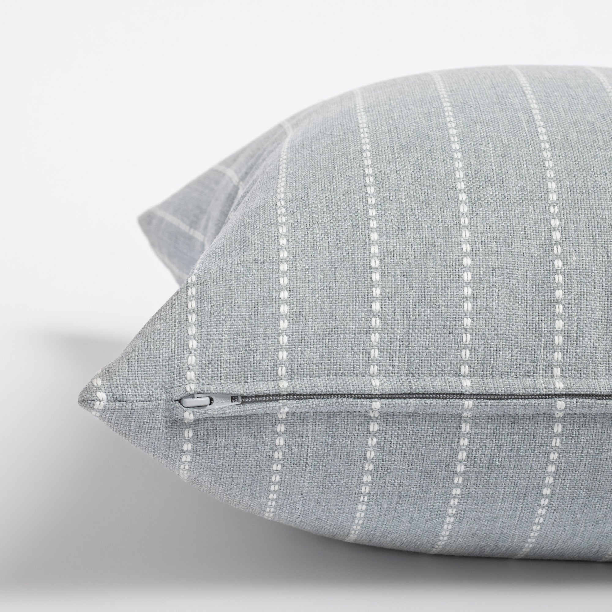 Fontana Cloud 20x20 pillow, a pale blue grey and white vertical stripe indoor outdoor pillow : close up zipper view