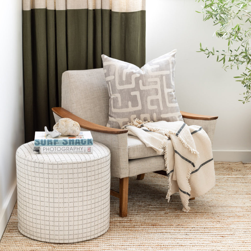 Keely Check Birch Round Ottoman used as a side table, Karru Silver pillow and Rafael Cream throw on armchair