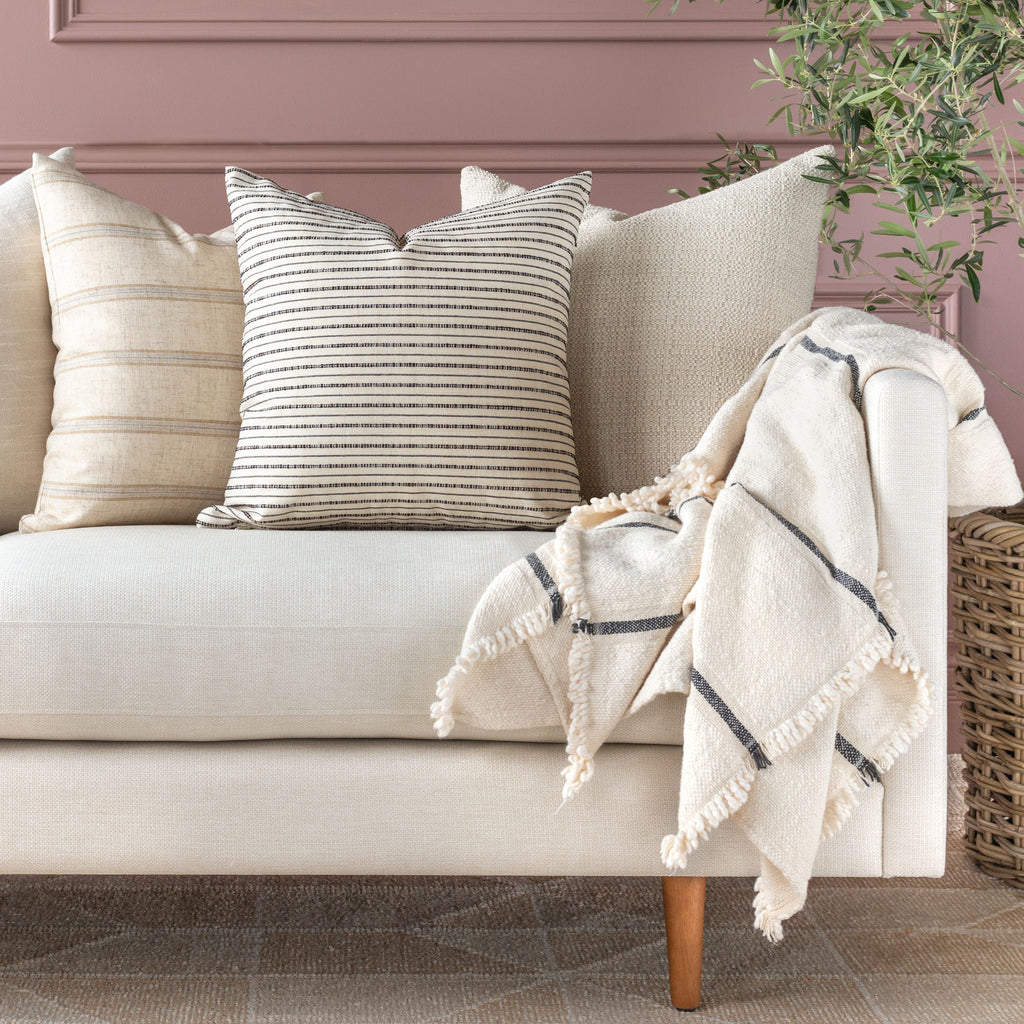 Cream sofa pillow combination : Misto cream and black stripe pillow with neutral pillows and cream tone throw blanket