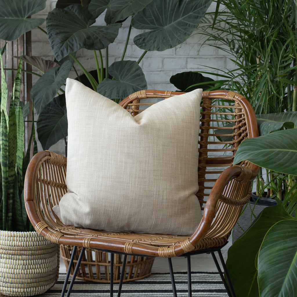 Ryder Swell beige pillow on a chair surrounded by plants